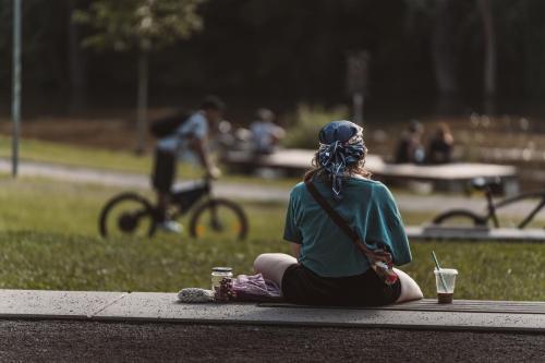 公園の段差に腰を下ろし、ひとりで過ごす女性の後ろ姿です。