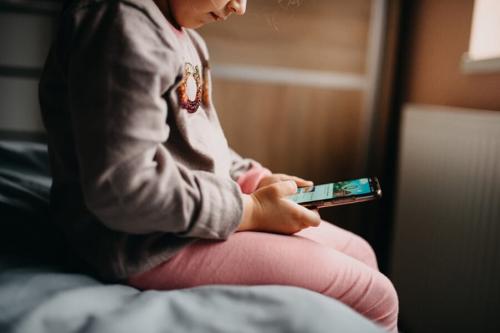 ベッドに座り、スマートフォンに見入る少女です。画面を延々とスクロールするうちに頭が腐っていくように感じる様子が、ブレインロットという言葉の意味です。