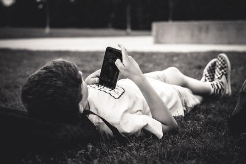 スマートフォンを手に、草の上に寝転ぶ男の子です(白黒写真)。ネット上の軽くて刺激の強い情報を大量に浴びる人に見られる頭の変化は、「ブレインロット」と呼ばれるようになりました。