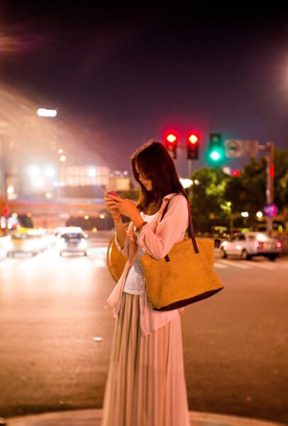 夜の屋外でスマートフォンを手にする女性です。AIの悪影響をよく言い当てたのは、投稿の長さではなく、いいねやリツイートの多さでした。