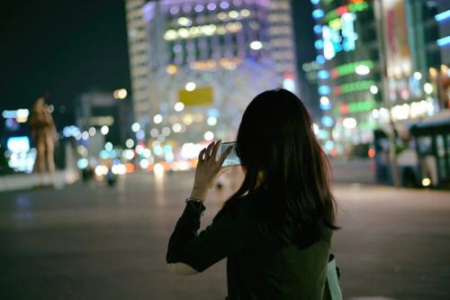 夜の街で、スマートフォンを使って写真を撮る女性です(韓国・ソウル)。のめり込み具合は、最初に用意した10問から、統計的な確認を経て残った6問で測られました。