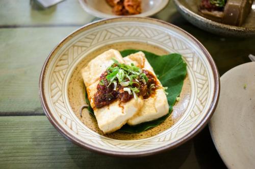 焼き色のついた豆腐に、赤いたれと刻んだネギをのせた料理。