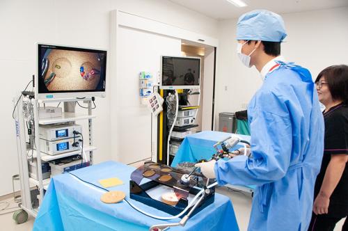 「腹腔鏡鉗子」を用いた作業を疑似体験する様子。遠隔モニター越しに患部に見立てたビーズを移し替える