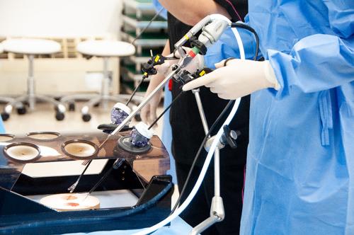「腹腔鏡鉗子」を用いた作業を疑似体験する様子。遠隔モニター越しに患部に見立てたビーズを移し替える