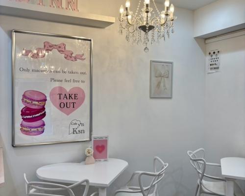 Cafe Ksyn'n(カフェ・カシノン)の白とピンクで統一された店内。店内に飾られているシャンデリアと、大きなピンクのマカロンが書かれたオリジナルポスター。