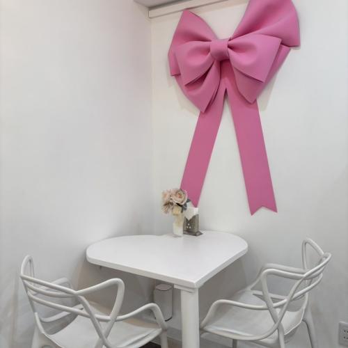 Cafe Ksyn'n(カフェ・カシノン)の店内の白い壁にディスプレイされたひと際大きなピンクのリボンの装飾とハート型のテーブル席