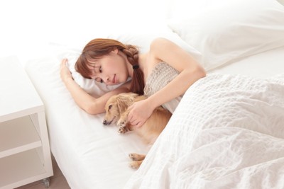 ベッドで横になる女性と犬