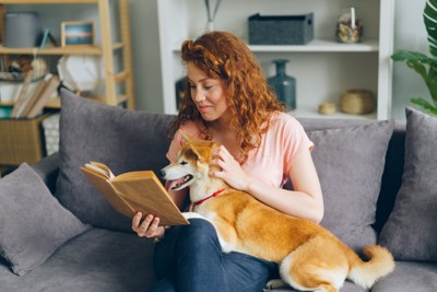 本を読みながら犬を撫でる女性