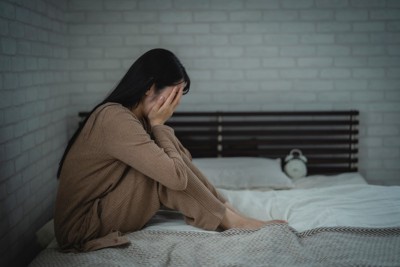 ベッドの上で顔を覆う女性
