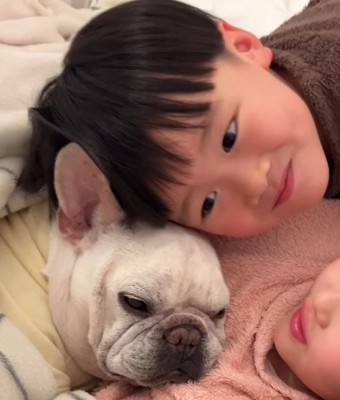 女の子に腕枕をされている犬を見つめる男の子