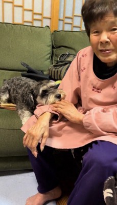 自分の腕にあごを乗せる犬を見て、笑顔になるおばあちゃん
