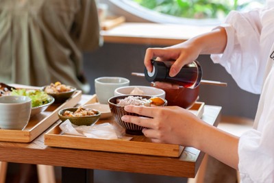 卵かけごはんにしょうゆをかける女性の手元