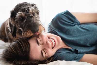 横たわる女性の耳元を舐める犬