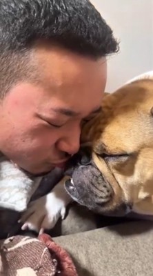 顔をくっつけて目を閉じている犬と男性